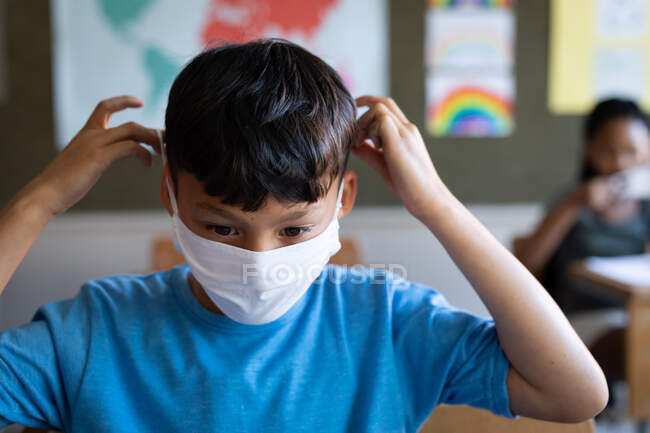 Смешанный расист в маске для лица, сидя на столе в школе. Начальное образование Социальное дистанцирование безопасности здоровья во время пандемии Coronavirus Covid19. — стоковое фото