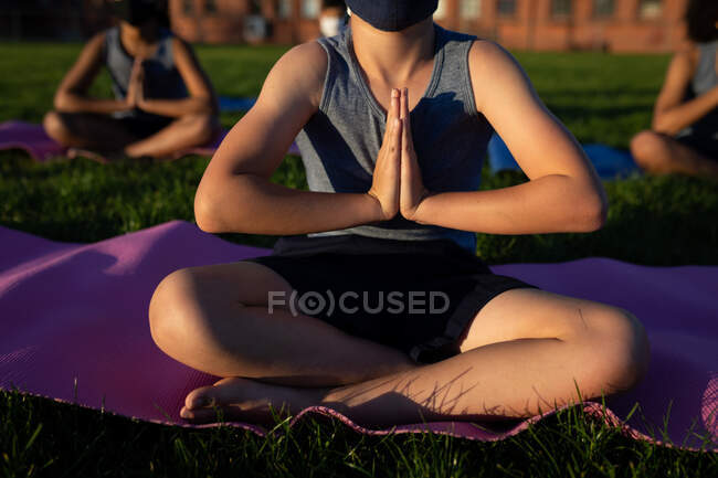 Mid section view of a group of multi ethnic kids wearing face masks performing yoga in the school garden. Primary education social distancing health safety during Covid19 Coronavirus pandemic. — Stock Photo