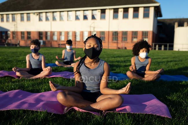 Grupo de crianças multi étnicas usando máscaras faciais realizando ioga no jardim da escola. Educação primária distanciamento social segurança sanitária durante Covid19 pandemia de coronavírus. — Fotografia de Stock