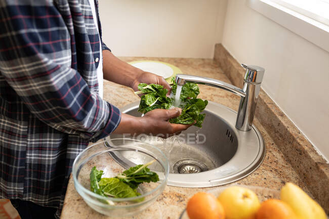 Hombre de pie en una cocina, lavando una col, distanciamiento social y auto aislamiento en cuarentena - foto de stock