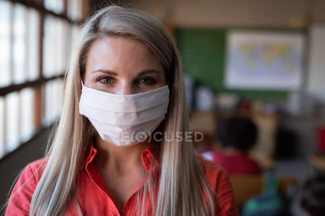 Porträt einer kaukasischen Lehrerin mit Mundschutz im Klassenzimmer. Grundschulbildung soziale Distanzierung der Gesundheitssicherheit während der Covid19 Coronavirus-Pandemie. — Stockfoto
