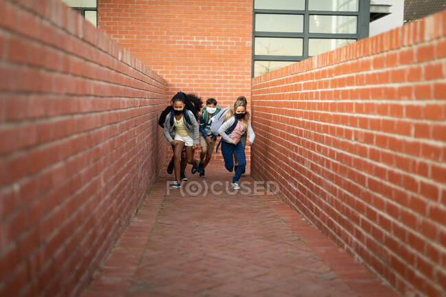 Grupo de niños multiétnicos con máscara facial corriendo durante un descanso. Educación primaria distanciamiento social seguridad sanitaria durante la pandemia del Coronavirus Covid19. - foto de stock