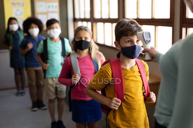 Professeure caucasienne mesurant la température des enfants dans une école primaire. Enseignement primaire distanciation sociale sécurité sanitaire pendant la pandémie de coronavirus Covid19. — Photo de stock