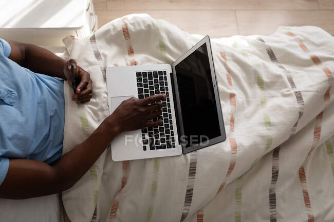 Чоловік лежить на ліжку в спальні, використовуючи ноутбук, соціальне дистанціювання та самоізоляцію в карантині — стокове фото