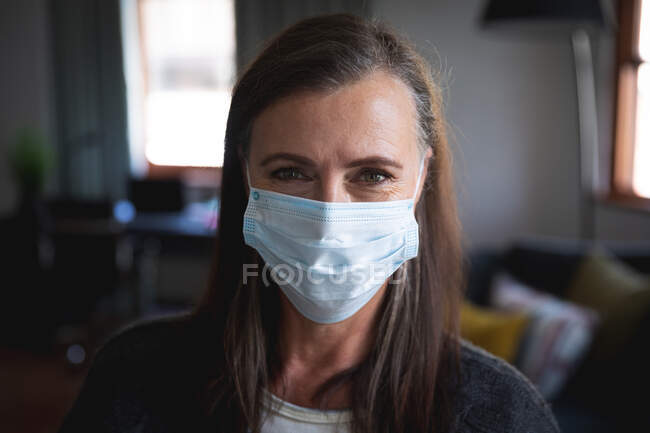 Портрет кавказької жінки, яка насолоджується перебуванням вдома, соціальною дистанцією і самоізоляцією під час карантинної блокування, одягнена маска для обличчя, що захищає від коронавірусної інфекції, дивлячись на камеру.. — стокове фото
