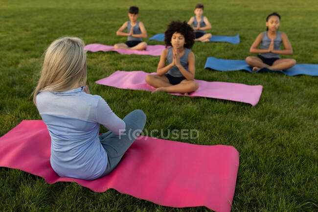Group of multi ethnic kids and their female teacher wearing face masks performing yoga in the school garden. Primary education social distancing health safety during Covid19 Coronavirus pandemic. — Stock Photo