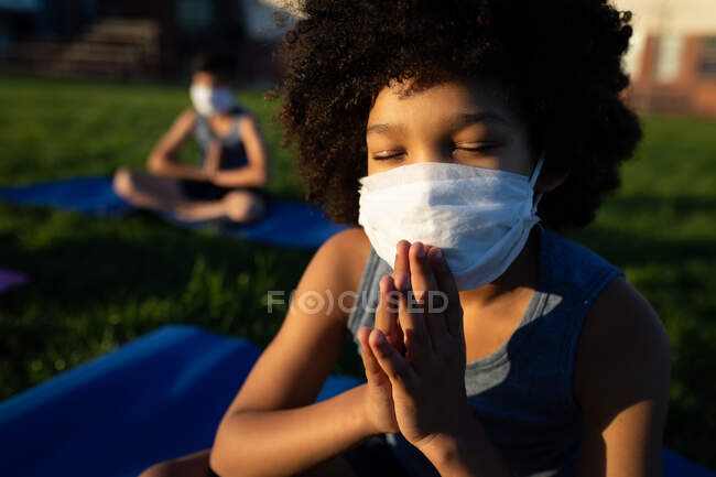 Menino de raça mista usando máscara facial realizando ioga no jardim da escola. Educação primária distanciamento social segurança sanitária durante Covid19 pandemia de coronavírus. — Fotografia de Stock