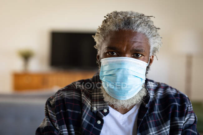Портрет афроамериканського старшого чоловіка сидячого, одягненого в маску обличчя, соціальну дистанцію і самоізоляцію в карантинному блокуванні. — стокове фото