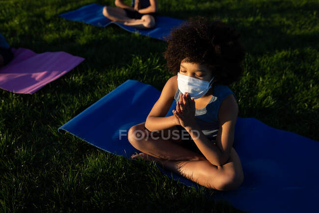 Vista aérea del niño con máscara facial realizando yoga en el jardín de la escuela. Educación primaria distanciamiento social seguridad sanitaria durante la pandemia del Coronavirus Covid19. - foto de stock