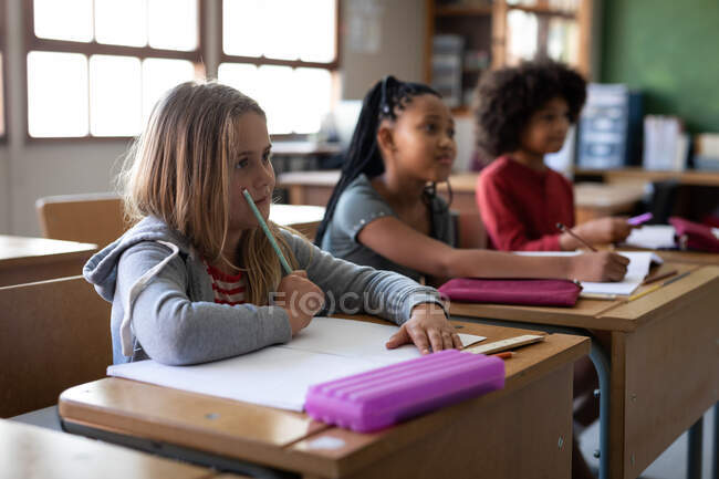 Grupo de crianças multi étnicas sentadas em sua mesa na sala de aula na escola. Educação primária distanciamento social segurança sanitária durante Covid19 pandemia de coronavírus. — Fotografia de Stock