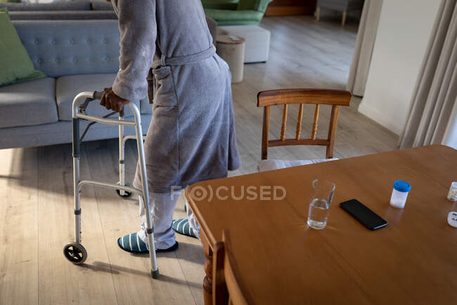 Hombre caminando, usando un andador, en una sala de estar, distanciamiento social y autoaislamiento en cuarentena - foto de stock