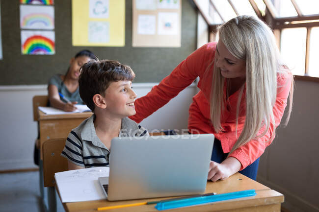 Female Caucasian teacher and a Caucasian boy using laptop during the lesson. Primary education social distancing health safety during Covid19 Coronavirus pandemic. — Stock Photo