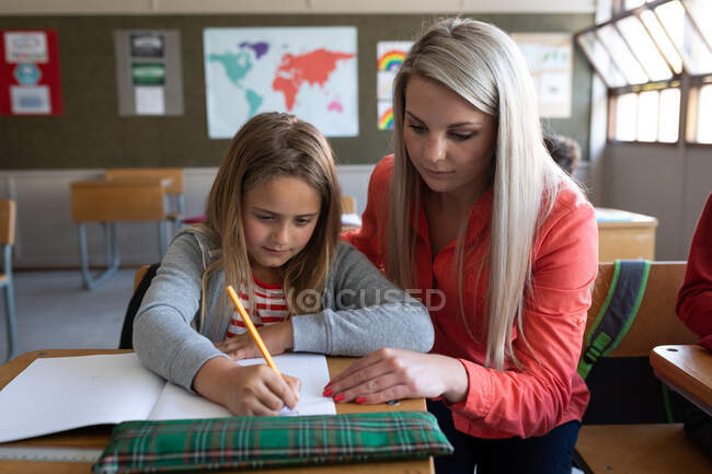 Insegnante caucasica che insegna a una ragazza caucasica durante la lezione. Istruzione primaria distanza sociale sicurezza sanitaria durante la pandemia di Covid19 Coronavirus. — Foto stock