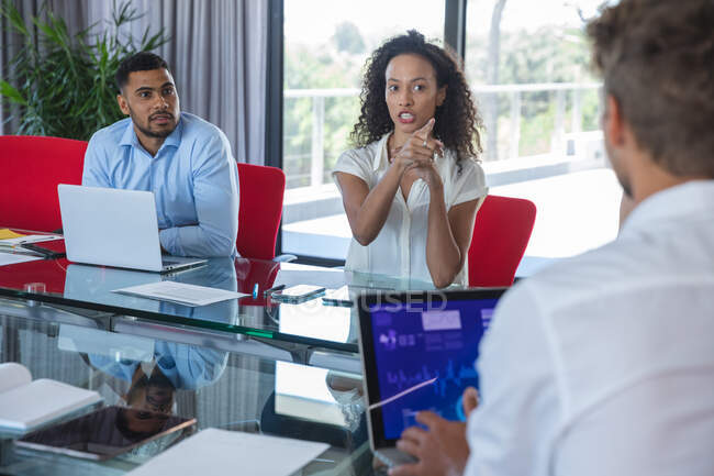 Mixed race businesswoman gesturing and talking during a business meeting, a mixed race male colleague sitting beside her listening. Creative business professionals working in a busy modern office. — Stock Photo