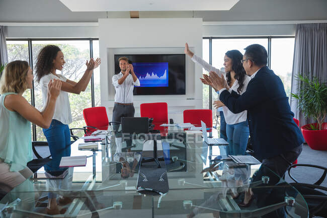 Multiethnische Gruppe von männlichen und weiblichen Geschäftskollegen, die am Ende eines Treffens stehen und klatschen und gemeinsam Erfolge feiern. Kreative Geschäftsprofis, die in einem modernen Büro arbeiten. — Stockfoto