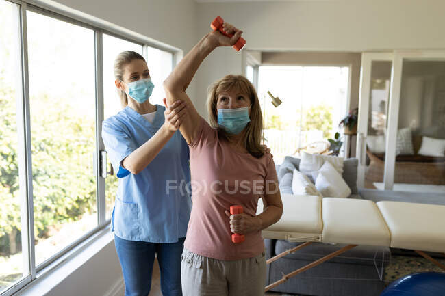 Старша кавказька жінка вдома, яку відвідала кавказька медсестра, розтягнула руку, одягнена в маски для обличчя. Медична допомога вдома під час карантину Covid 19 Coronavirus. — стокове фото