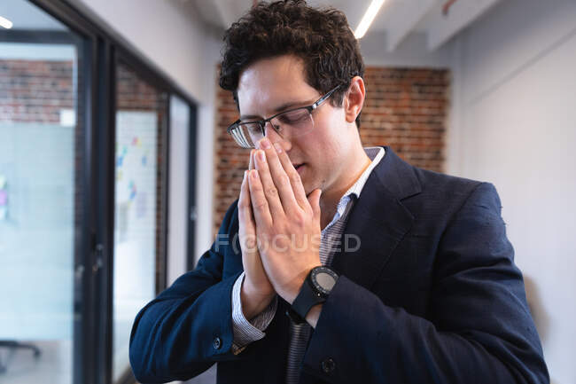 Hombre caucásico trabajando en una oficina informal, estornudando y cubriéndose la nariz. Distanciamiento social en el lugar de trabajo durante la pandemia de Coronavirus Covid 19. - foto de stock