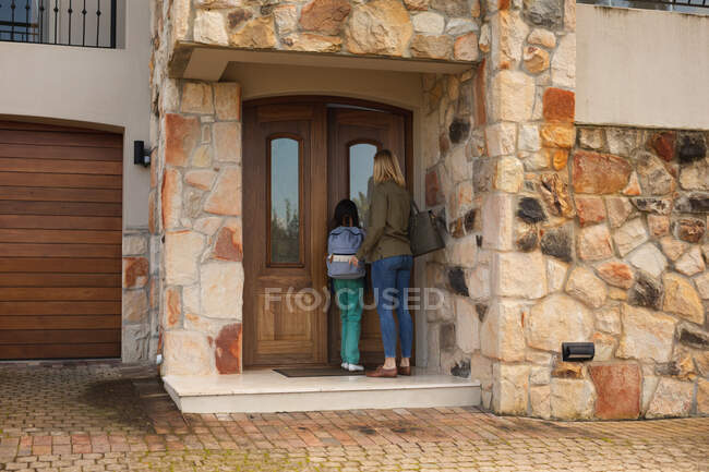 Белая женщина и её дочь входят в дом, открывая дверь. Социальное дистанцирование во время изоляции коронавируса Covid 19. — стоковое фото