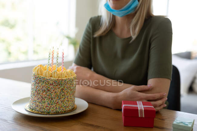 Кавказька жінка проводить час удома, сидячи у вітальні з тортом до дня народження і даруючи його на столі. Соціальна дистанція під час карантину Ковида 19.. — стокове фото
