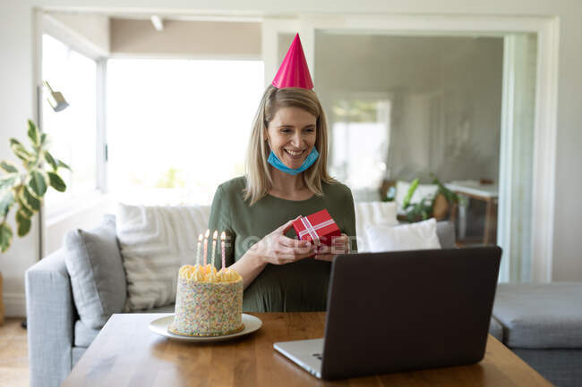 Caucasian woman spending time at home, sitting in living room with birthday cake and using laptop. Social distancing during Covid 19 Coronavirus quarantine. — Stock Photo