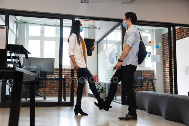 Mixed race woman and Caucasian man working in a casual office, wearing face masks and touching each other legs. Social distancing in the workplace during Coronavirus Covid 19 pandemic. — Stock Photo