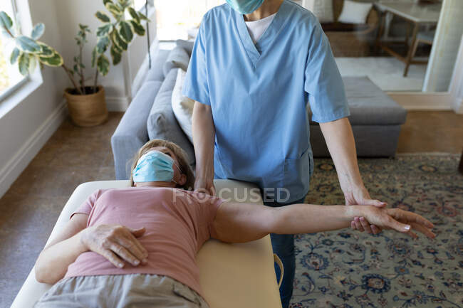 Eine ältere kaukasische Frau zu Hause, die von einer kaukasischen Krankenschwester besucht wird, streckt ihren Arm aus und trägt Gesichtsmasken. Medizinische Versorgung zu Hause während der Quarantäne des Covid 19 Coronavirus. — Stockfoto