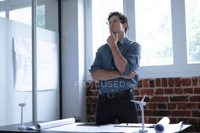 Kaukasischer Mann, der in einem lässigen Büro arbeitet, an seinem Schreibtisch steht und nachdenkt. Soziale Distanzierung am Arbeitsplatz während der Coronavirus Covid 19 Pandemie. — Stockfoto