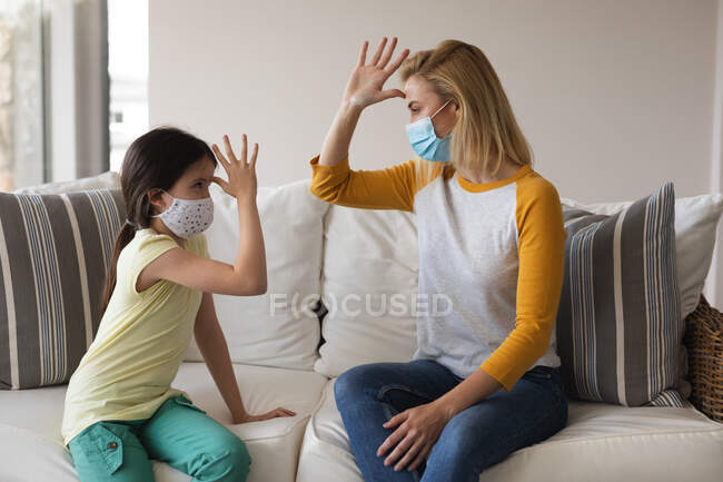 Mulher caucasiana e sua filha passam o tempo em casa juntas, usando máscaras faciais, conversando usando linguagem gestual. Distanciamento social durante o bloqueio de quarentena do Covid 19 Coronavirus. — Fotografia de Stock