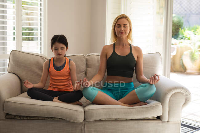 Donna caucasica e sua figlia passano del tempo a casa insieme, facendo yoga, meditando. Distanza sociale durante il blocco di quarantena Covid 19 Coronavirus. — Foto stock