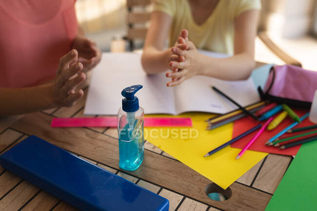 Woman and her daughter spending time at home together, disinfecting their hands,  doing schoolwork. Social distancing during Covid 19 Coronavirus quarantine lockdown. — Stock Photo