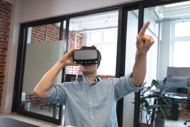 Caucasian man working in a casual office, wearing vr headset, touching virtual screen. Social distancing in the workplace during Coronavirus Covid 19 pandemic. — Stock Photo
