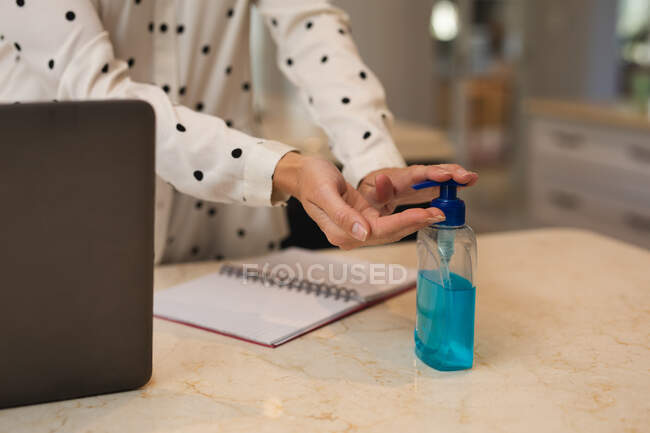 Woman working from home, disinfecting her hands. Social distancing during Covid 19 Coronavirus quarantine lockdown. — Stock Photo