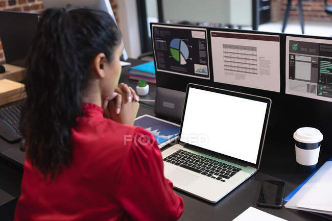 Gemischte Rassenfrau, die in einem Gelegenheitsbüro arbeitet, am Schreibtisch sitzt und einen Laptop benutzt. Soziale Distanzierung am Arbeitsplatz während der Coronavirus Covid 19 Pandemie. — Stockfoto