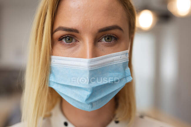 Retrato de mulher caucasiana passando tempo em casa, usando máscara facial, olhando para a câmera. Distanciamento social durante o bloqueio de quarentena do Covid 19 Coronavirus. — Fotografia de Stock