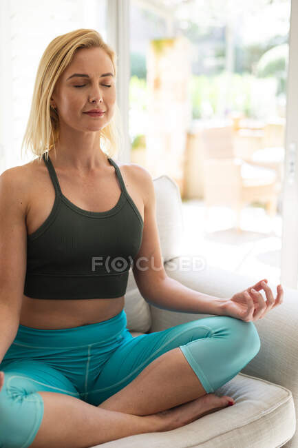 Mujer caucásica pasando tiempo en casa, haciendo yoga, meditando. Distanciamiento social durante el bloqueo de cuarentena del Coronavirus Covid 19. - foto de stock