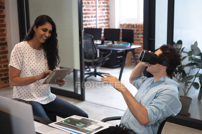 Mixed race woman and Caucasian man working in a casual office, the man wearing vr headset and the woman using a tablet. Creative business professionals working in a busy modern office. — Stock Photo