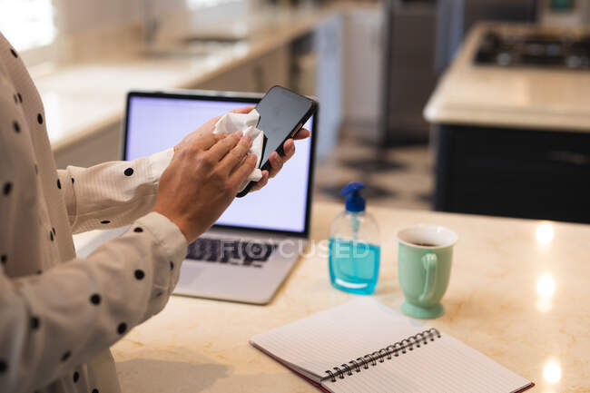 Mulher trabalhando em casa, limpando seu smartphone e usando computador portátil. Distanciamento social durante o bloqueio de quarentena do Covid 19 Coronavirus. — Fotografia de Stock