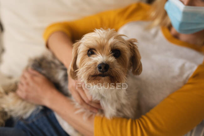 Mulher passar o tempo em casa, usando máscara facial, abraçando seu cão. Distanciamento social durante o bloqueio de quarentena do Covid 19 Coronavirus. — Fotografia de Stock