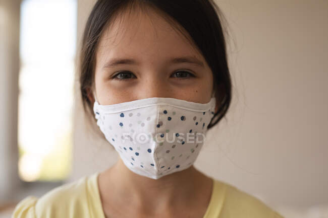 Portrait of Caucasian girl spending time at home, wearing face mask, looking at camera. Social distancing during Covid 19 Coronavirus quarantine lockdown. — Stock Photo