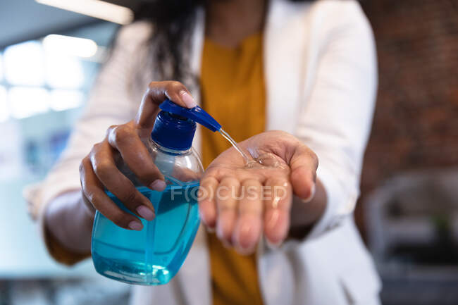 Gros plan d'une femme travaillant dans un bureau décontracté, utilisant un désinfectant. Distance sociale sur le lieu de travail pendant la pandémie de coronavirus Covid 19. — Photo de stock