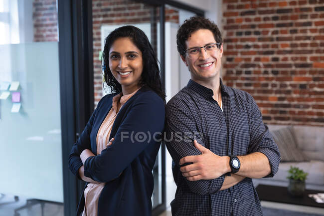 Portrait of mixed race woman and Caucasian man working in a casual office, smiling and looking at camera. Creative business professionals working in a busy modern office. — Stock Photo