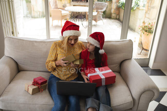 Caucasian woman and her daughter spending time at home together, wearing santa hats, using a laptop computer, making a video call. Social distancing during Covid 19 Coronavirus quarantine lockdown. — Stock Photo