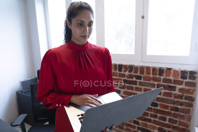 Mixed race woman working in a casual office, using a laptop computer. Social distancing in the workplace during Coronavirus Covid 19 pandemic. — Stock Photo