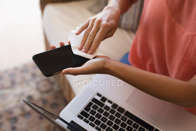 Donna che lavora da casa, pulisce il suo smartphone e utilizza il computer portatile. Distanza sociale durante il blocco di quarantena Covid 19 Coronavirus. — Foto stock