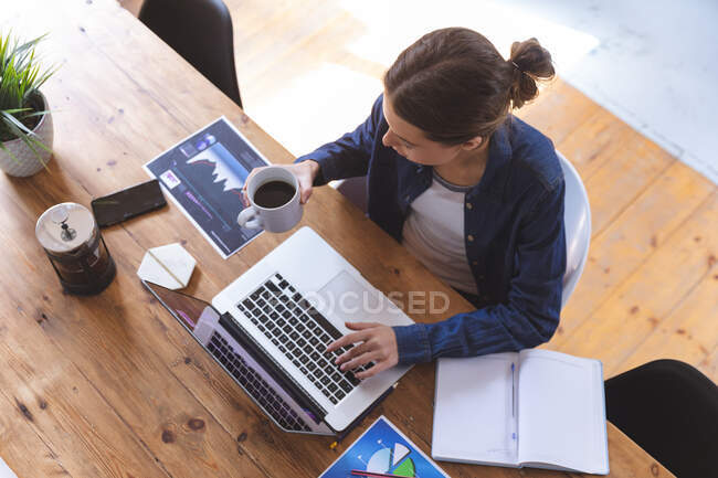 Caucasian woman spending time at home, sitting by table in kitchen using laptop computer, working from home, holding mug. Social distancing during Covid 19 Coronavirus quarantine lockdown. — Stock Photo