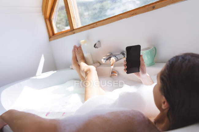 Кавказька жінка проводить час удома, у ванній кімнаті, лежачи в ванній, розслабившись від чашки. Соціальна дистанція в Ковиді 19 Коронавірус карантин. — стокове фото