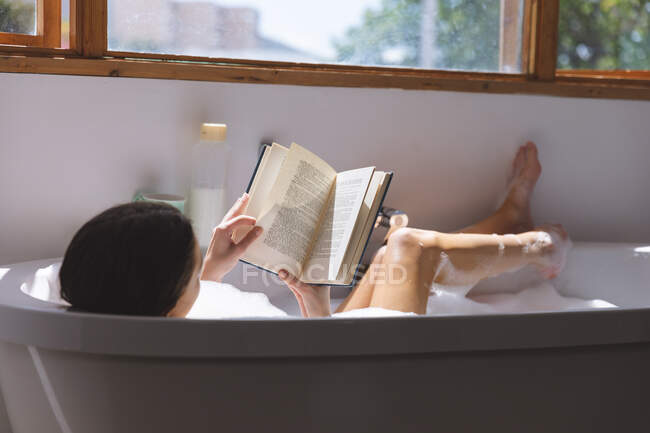 Kaukasische Frau verbringt Zeit zu Hause, im Badezimmer, in der Badewanne liegend, Buch lesend. Soziale Distanzierung während Covid 19 Coronavirus Quarantäne Lockdown. — Stockfoto