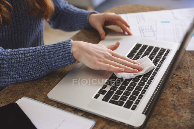 Mulher caucasiana passando tempo em casa, na cozinha, trabalhando em casa, usando seu laptop, limpando seu laptop. Distanciamento social durante o bloqueio de quarentena do Covid 19 Coronavirus. — Fotografia de Stock