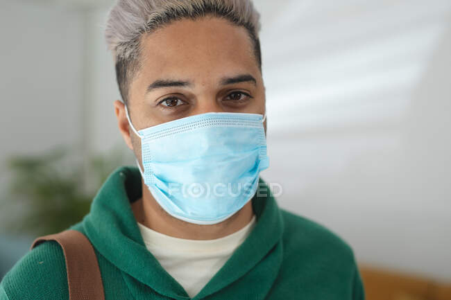 Porträt eines männlichen Geschäftsmannes mit gemischter Rasse, der in einem Büro mit Gesichtsmaske steht. Gesundheit und Hygiene am Arbeitsplatz während der Coronavirus Covid 19 Pandemie. — Stockfoto