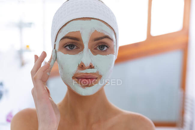 Portrait of Caucasian woman spending time at home, standing in bathroom, looking at camera applying face mask. Social distancing during Covid 19 Coronavirus quarantine lockdown. — Stock Photo